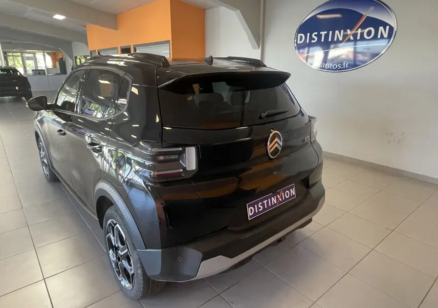 Vue 3/4 arrière droite d'une Citroën E-C3 113 MAX noire électrique, avec jantes alliage et vitres arrière surteintées en showroom.