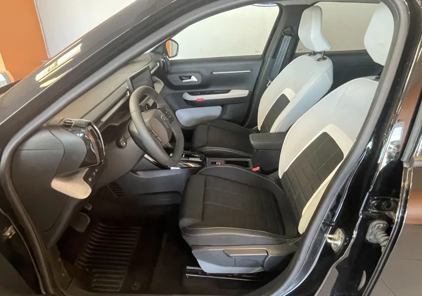 Vue intérieure côté conducteur de la Citroën E-C3 113 MAX noire, avec sièges bicolores tissu clair et noir.