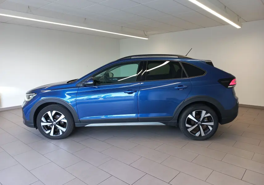 Vue de profil côté gauche d'un Volkswagen Taigo bleu récif avec jantes alliage 17 pouces dans un intérieur lumineux.