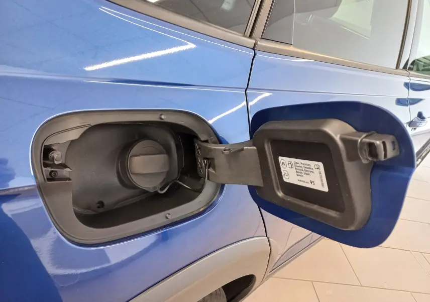 Gros plan sur la trappe à carburant ouverte côté gauche du Volkswagen Taigo bleu récif, montrant le bouchon essence et l’étiquette.