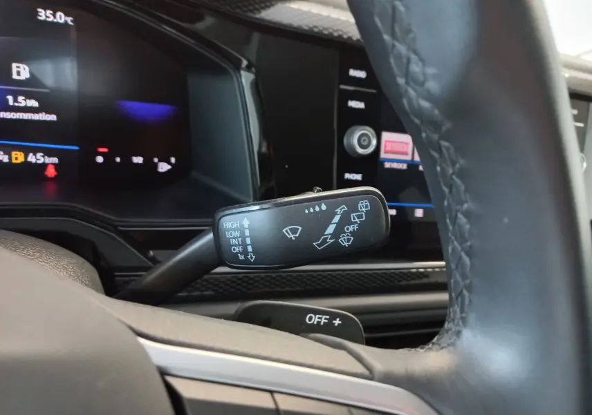 Gros plan sur le commodo d’essuie-glace du Volkswagen Taigo 2025, intérieur noir avec tableau de bord numérique.