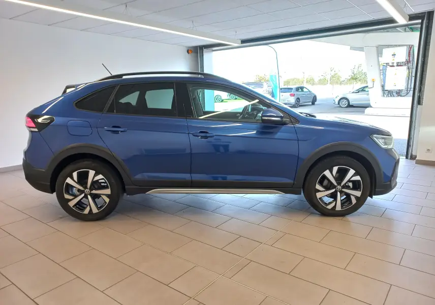 Vue de profil côté gauche d'un Volkswagen Taigo 2025 bleu récif avec jantes alliage 17 pouces Aberdeen en intérieur showroom.