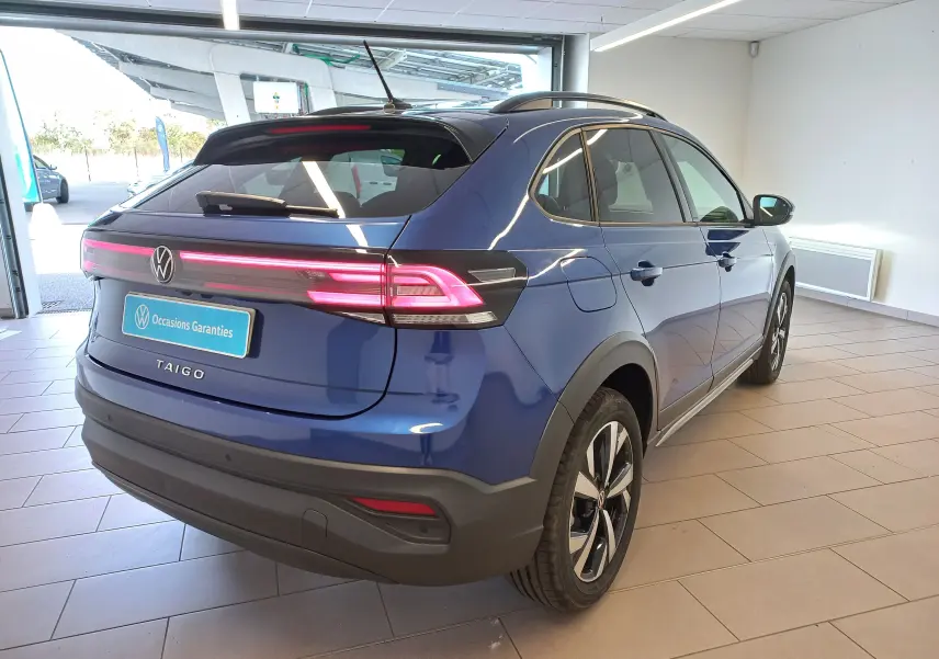 Vue 3/4 arrière droite du Volkswagen Taigo bleu récif avec feux arrière allumés et jantes alliage Aberdeen 17 pouces.