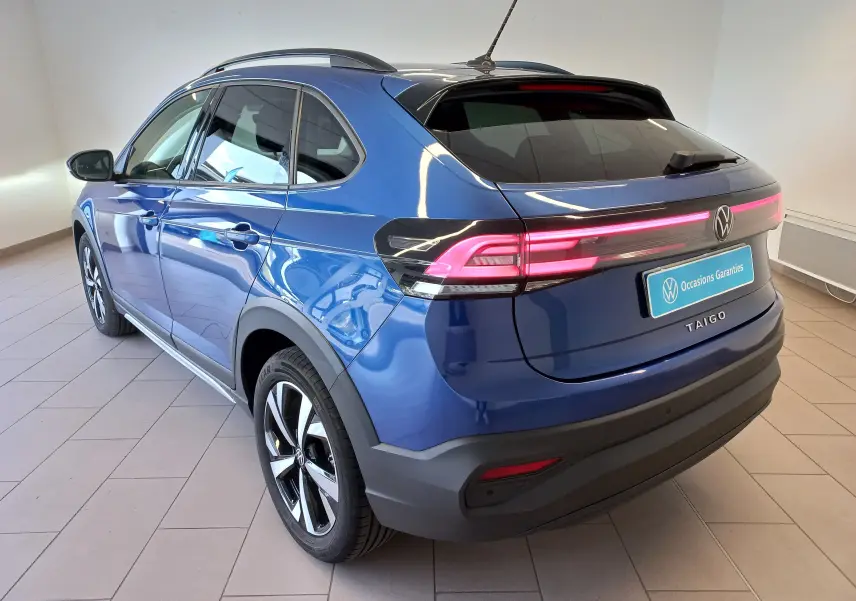 Vue 3/4 arrière droite du Volkswagen Taigo bleu récif avec feux arrière allumés et jantes alliage Aberdeen 17 pouces.