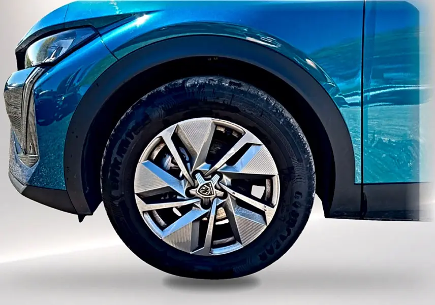Gros plan sur la roue avant gauche bleu métallisé d'une Peugeot 408 Hybrid 145 allure avec jante alu au design moderne.