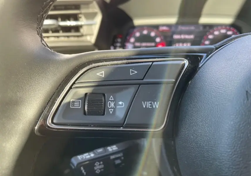 Gros plan sur les commandes au volant de l'Audi A3 2022, finition confort, tableau de bord digital en arrière-plan flou.