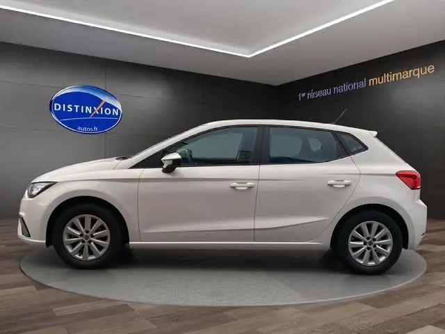 Profil côté gauche d'une SEAT IBIZA 2023 blanc candy, compacte cinq portes, sur un plateau en showroom.