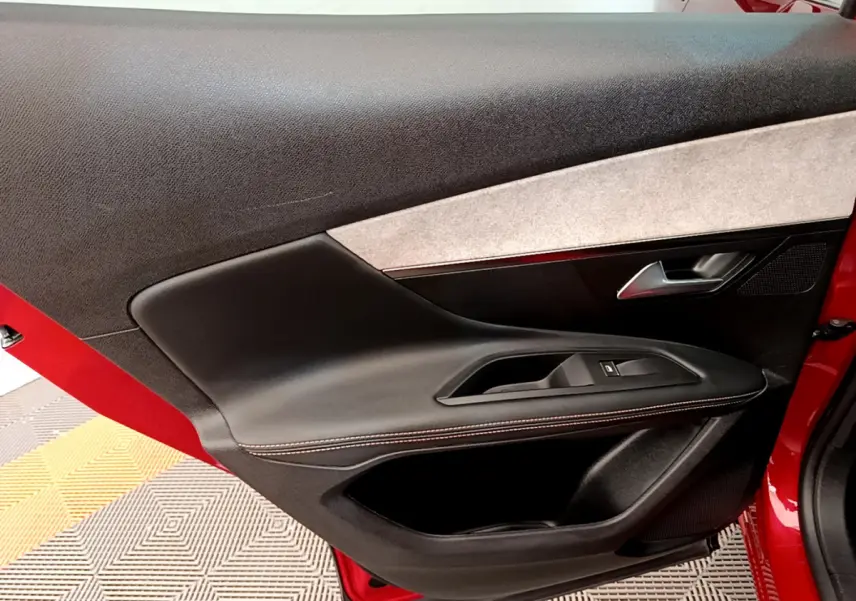 Gros plan sur la porte avant gauche rouge du Peugeot 3008 GT avec garniture noire et insert tissu clair.