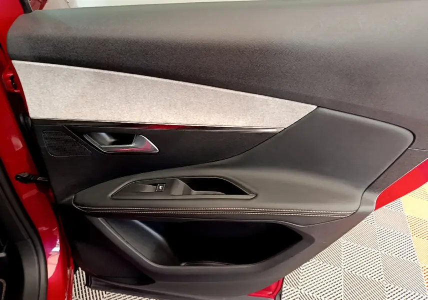 Vue rapprochée de la porte avant gauche rouge du Peugeot 3008 GT avec garniture noire et grise et bouton de fenêtre électrique.