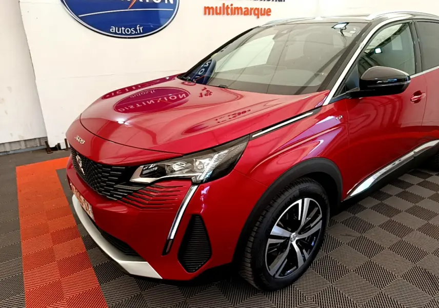 Vue 3/4 avant d'un Peugeot 3008 GT rouge avec phares LED et jantes alliage bicolores dans un showroom.