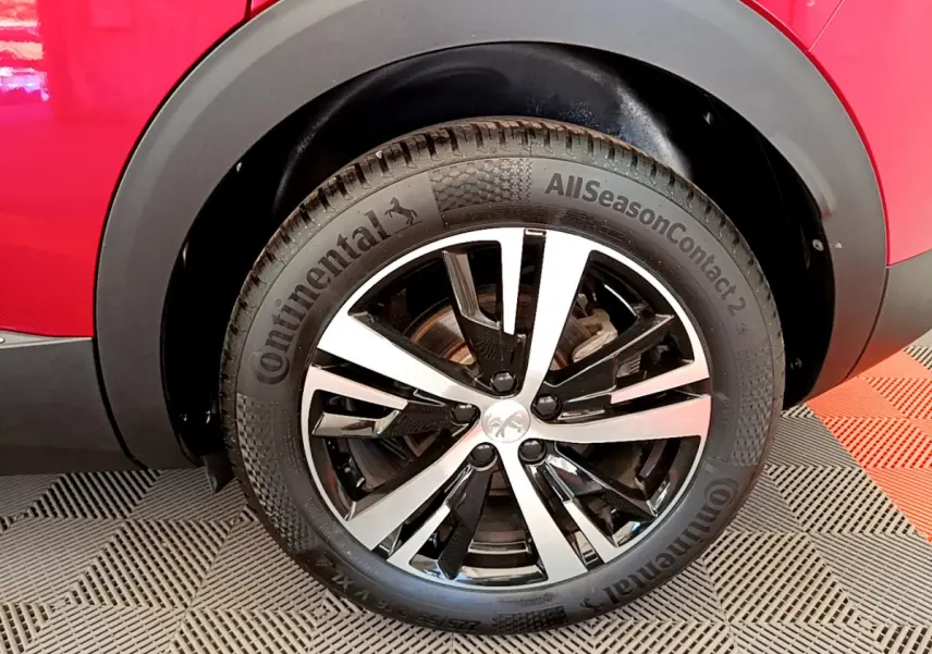 Gros plan sur la roue avant droite d’un Peugeot 3008 rouge avec jante alliage bicolore et pneu Continental.