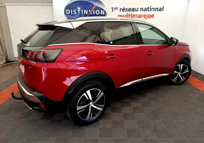 Vue 3/4 arrière droite d'un Peugeot 3008 GT rouge avec toit noir et jantes alliage bicolores dans un showroom.