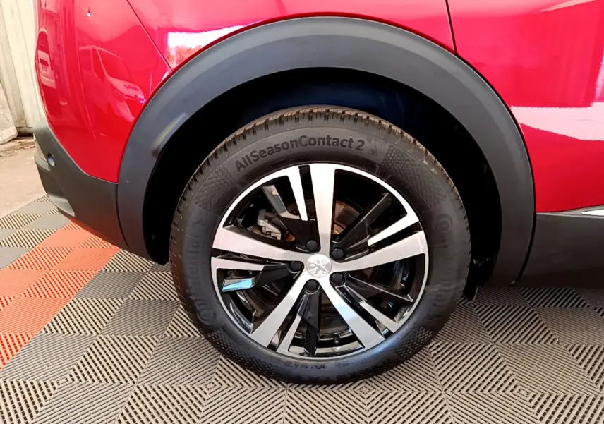 Gros plan sur la roue arrière droite d'un Peugeot 3008 rouge avec jante alliage bicolore et pneu Continental.