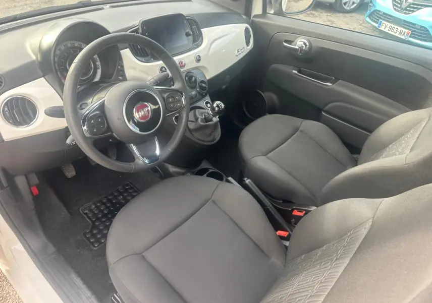 Vue intérieure côté conducteur de la Fiat 500 blanche 2023, avec tableau de bord clair et boîte manuelle visible.