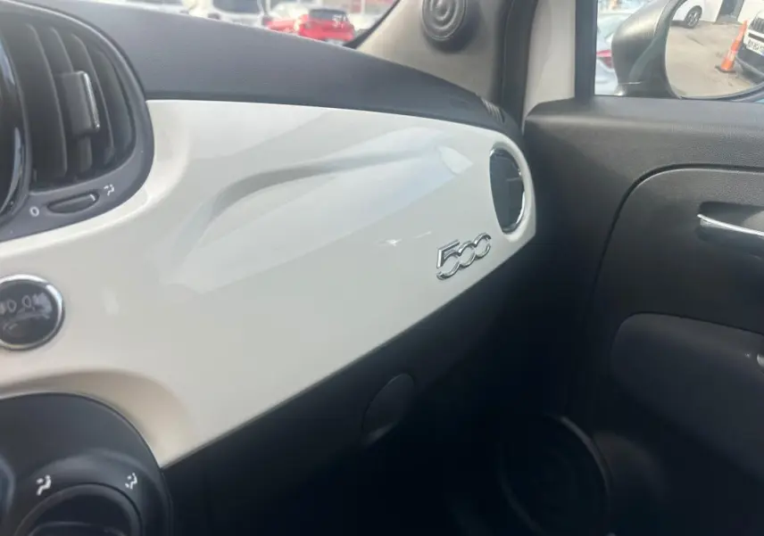 Vue intérieure côté passager du tableau de bord blanc brillant d'une Fiat 500 avec logo 500 visible sur la planche.