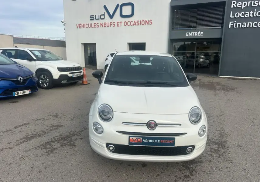 Vue de face d'une FIAT 500 blanche 2023, avec logo FIAT visible et plaque "Véhicule récent" sur un parking de concession.