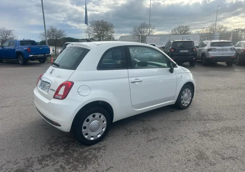 Vue 3/4 arrière droite d'une FIAT 500 blanche de 2023, version hybride essence, garée en extérieur sur un parking.
