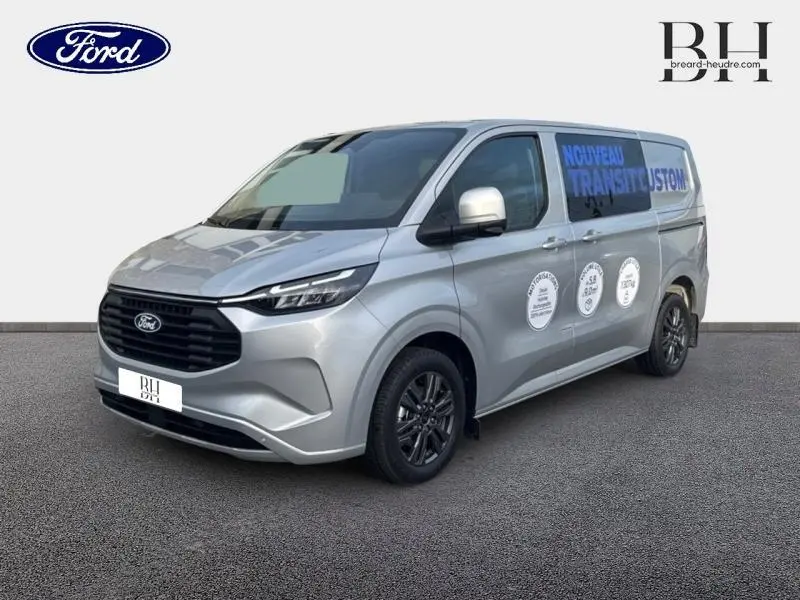 Ford Transit Custom gris lunaire métallisé vu en 3/4 avant droit avec marquages publicitaires sur la porte latérale.