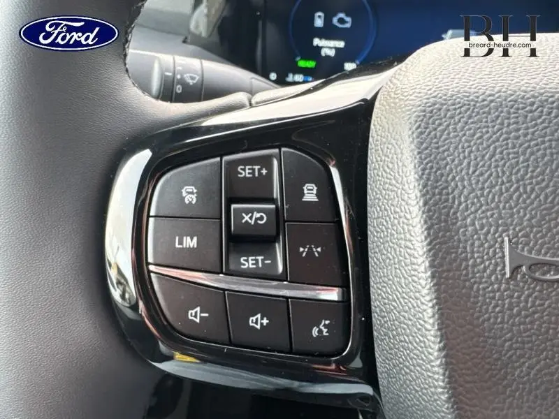 Gros plan sur les commandes au volant noir du Ford Transit Custom Fourgon, boutons multifonctions visibles côté gauche.