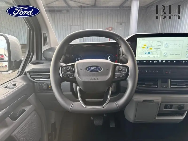 Vue intérieure frontale du volant et tableau de bord du Ford Transit Custom gris lunaire avec écran tactile et commandes intégrées.