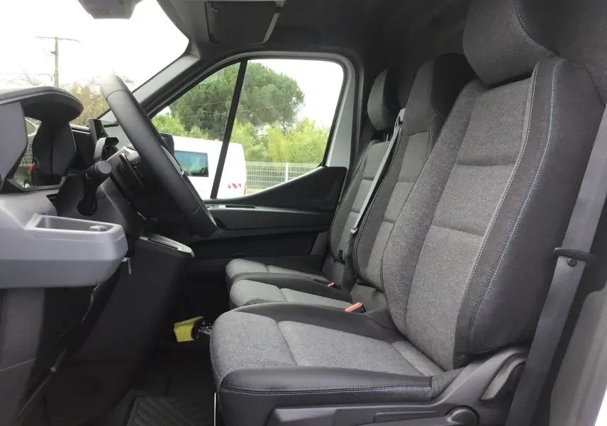 Vue intérieure côté droit du Renault Master 2026 blanc, montrant les trois sièges avant en tissu gris avec coutures bleues.