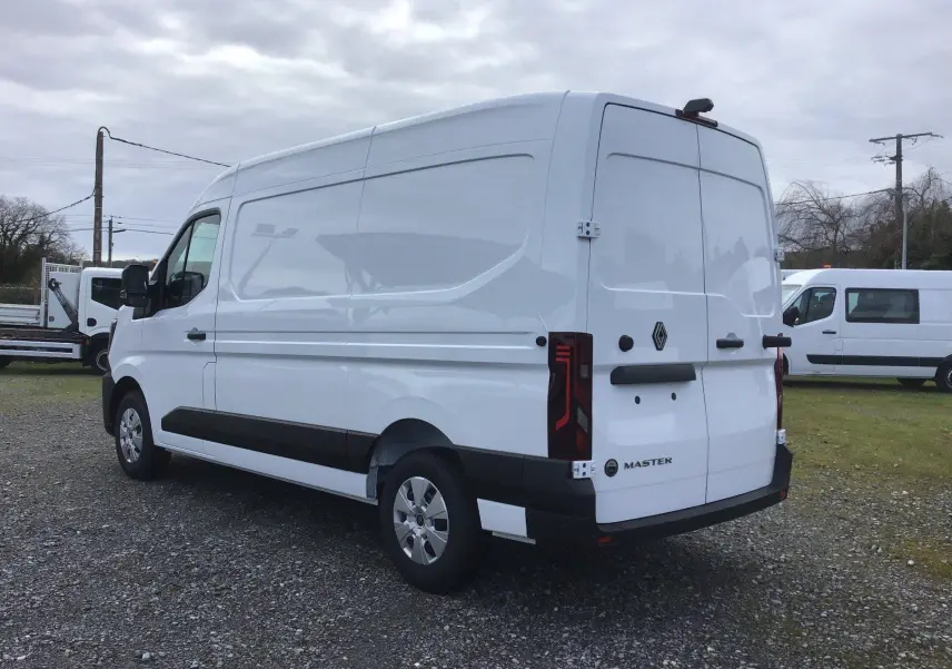 Vue 3/4 arrière droite d’un utilitaire Renault Master blanc avec portes arrière fermées sur un sol gravillonné.