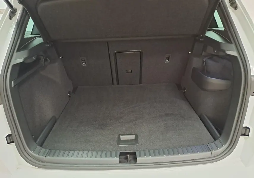 Coffre ouvert d’un Skoda Karoq 2025 blanc lune, vue de l’arrière montrant un espace de chargement spacieux et tapis gris.
