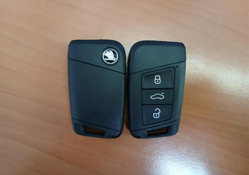 Clé de voiture SKODA KAROQ 1.5 TSI 150 DSG7 SPORTLINE 2025 en noir, vue de face et dos sur fond bois.