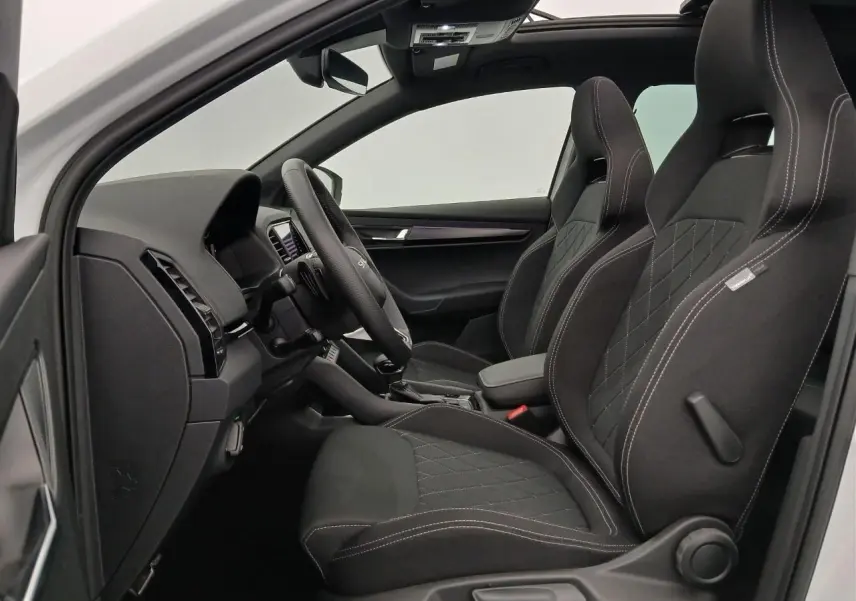 Vue intérieure côté gauche du Skoda Karoq 1.5 TSI 150 DSG7 Sportline 2025 en Blanc Lune, sièges sport noirs avec surpiqûres.