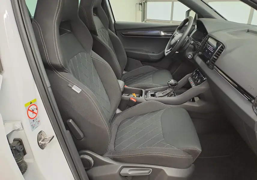Vue intérieure côté gauche du Skoda Karoq 2025 blanc lune, mettant en valeur les sièges sport noirs avec surpiqûres contrastées.