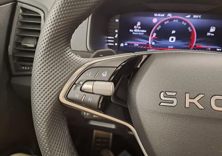 Gros plan sur le volant perforé et les commandes multifonctions du Skoda Karoq 1.5 TSI 150 DSG7 Sportline, tableau de bord numérique visible.