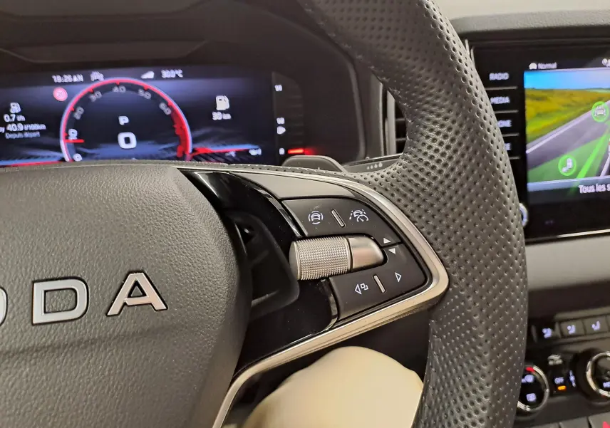 Gros plan sur le volant perforé du Skoda Karoq 2025 blanc lune, avec commandes multifonctions et tableau de bord numérique.