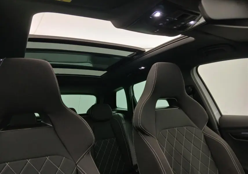 Intérieur du Skoda Karoq 2025 blanc lune, vue avant sur les sièges sport noirs avec surpiqûres blanches et toit panoramique ouvert.