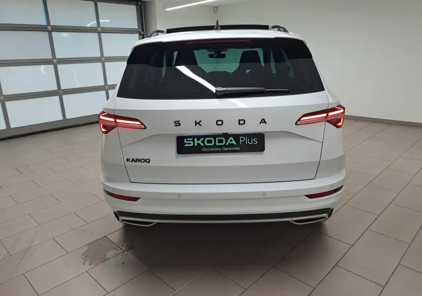 Vue arrière d'un Skoda Karoq blanc lune 2025 avec feux LED allumés et double sortie d'échappement intégrée au pare-chocs.