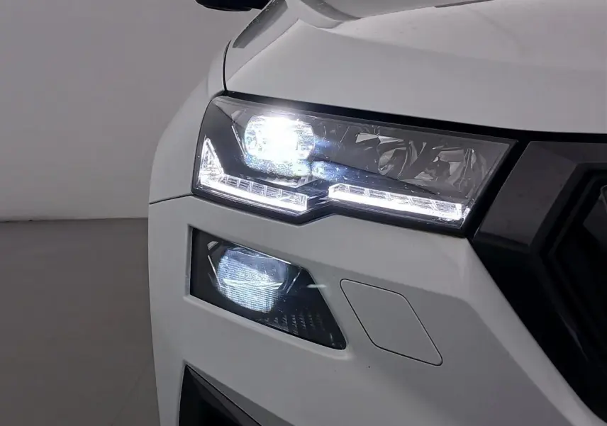 Gros plan sur le phare avant gauche allumé du Skoda Karoq 2025 blanc lune version Sportline.