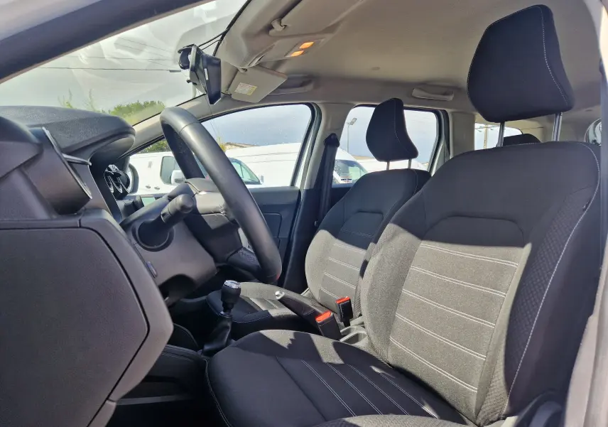 Intérieur du Dacia Duster 2023 vu côté conducteur, sièges noirs avec surpiqûres blanches et volant multifonction.