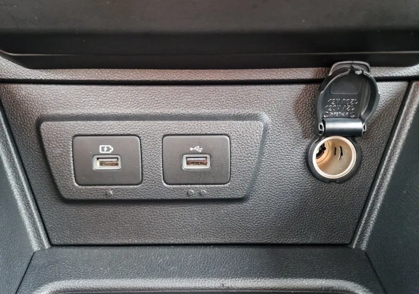 Vue rapprochée des prises USB et de l’allume-cigare sur la console centrale noire du Dacia Duster blanc 2023.