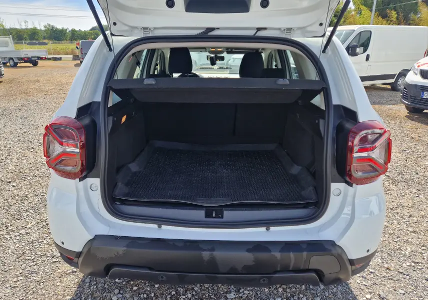 Vue arrière du Dacia Duster blanc 2023 avec coffre ouvert montrant l'espace de chargement et la plage arrière.