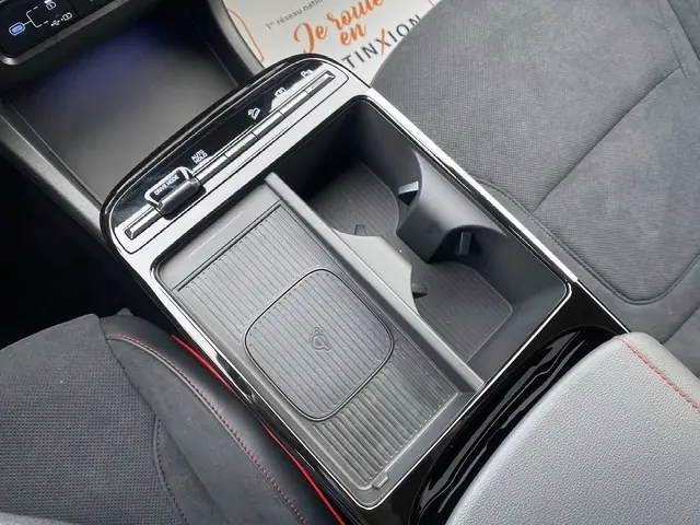 Gros plan sur la console centrale noire du Hyundai Tucson gris foncé, avec zone de recharge par induction et porte-gobelets.