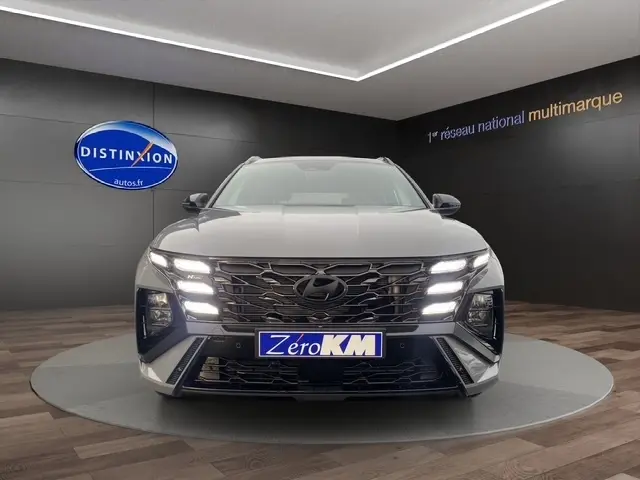 Vue frontale d'un Hyundai Tucson gris foncé 2026 avec feux LED allumés et calandre imposante en showroom.