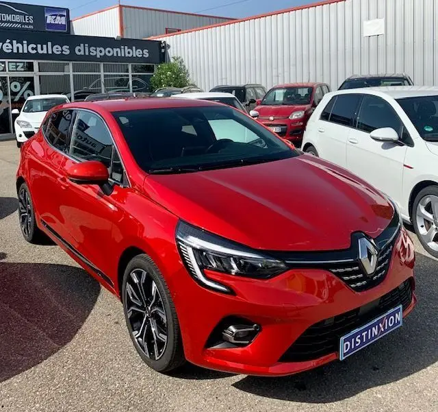 Renault Clio V rouge vue 3/4 avant droit, avec phares LED et jantes alliage distinctives, stationnée en extérieur.