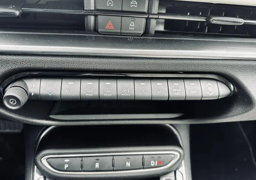 Gros plan sur la console centrale de la Fiat 600 La Prima 2024, montrant les commandes de climatisation et la boîte auto noire.
