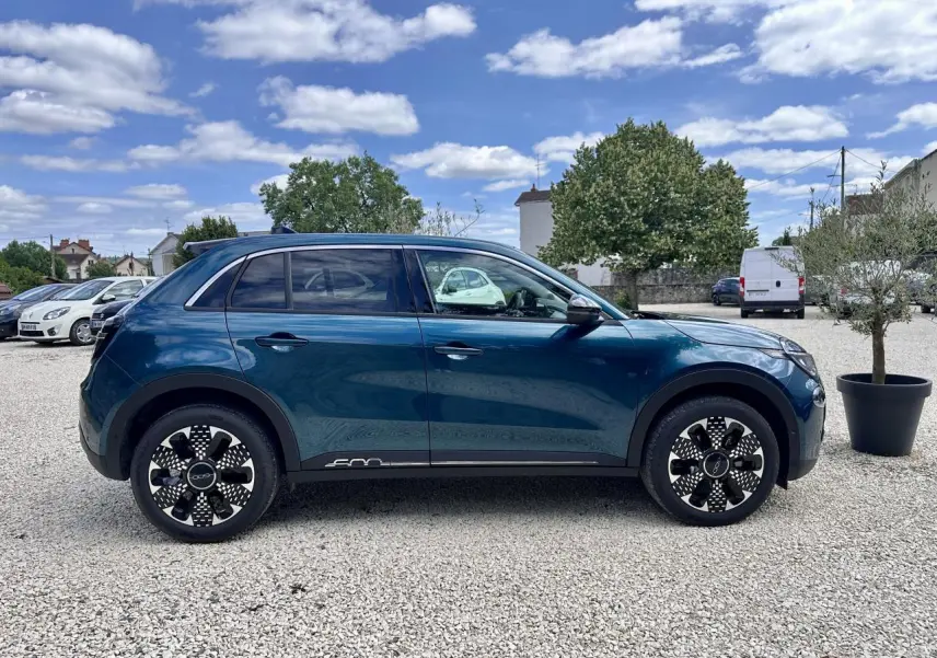 Vue de profil côté gauche d'une FIAT 600 1.2 Hybrid bleu clair avec jantes noires et détails blancs sur un parking extérieur.