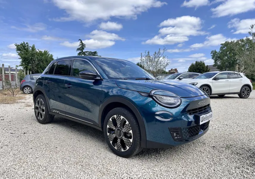 Vue 3/4 avant droite d'une FIAT 600 bleu clair avec jantes stylisées et calandre noire en extérieur.
