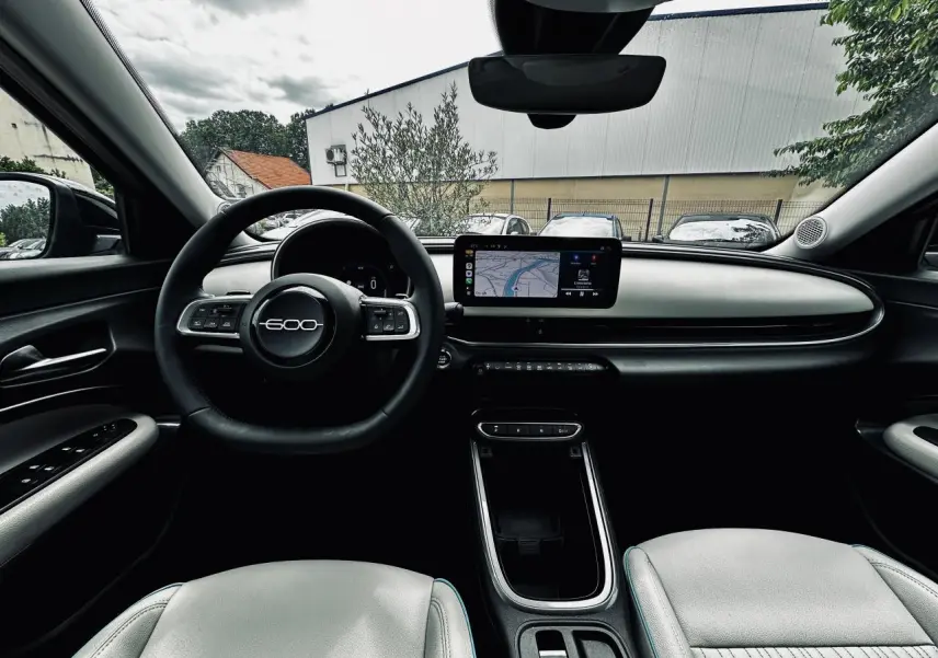 Vue intérieure avant du Fiat 600 La Prima 2024, planche de bord ivoire avec écran tactile et volant marqué 600.