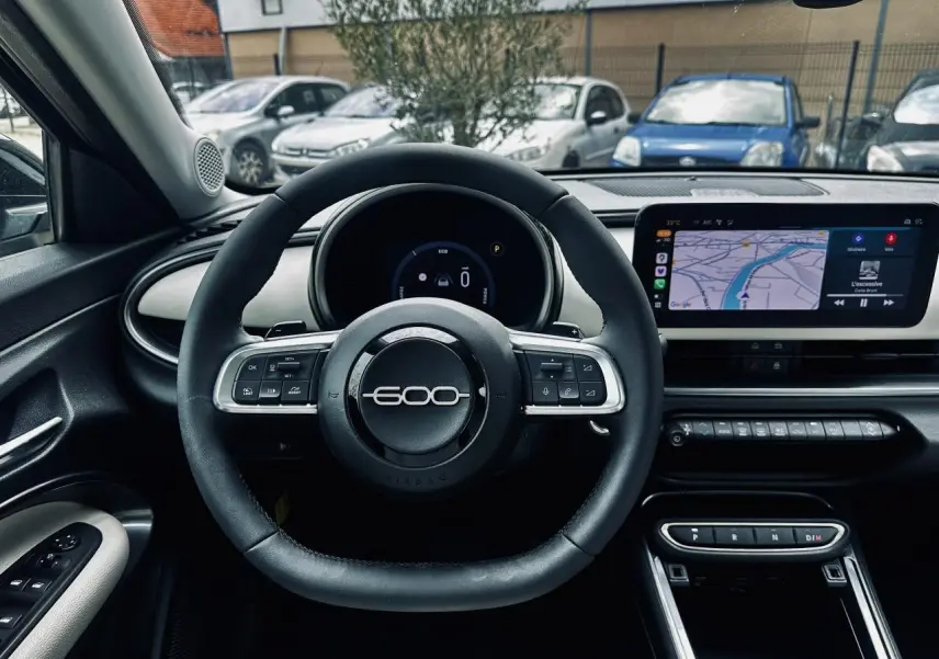 Vue intérieure centrée sur le volant noir marqué 600 et l'écran tactile du tableau de bord de la Fiat 600 bleu clair 2024.