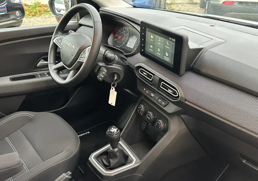 Vue intérieure côté conducteur du tableau de bord noir et gris du Dacia Sandero blanc avec écran tactile et boîte manuelle.