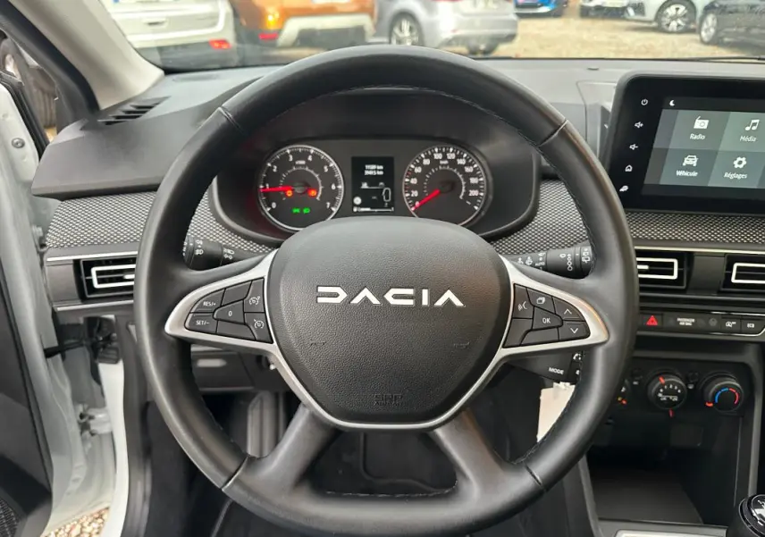 Vue intérieure centrée sur le volant noir de la Dacia Sandero 2024 avec tableau de bord et écran tactile visible.