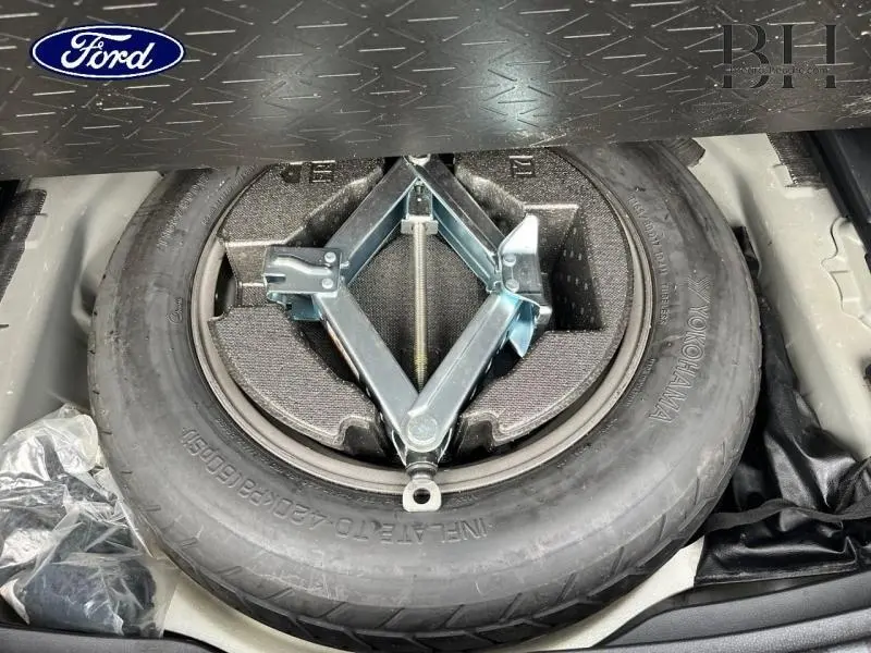 Vue plongeante sur la roue de secours noire et le cric métallique dans le coffre d’un Toyota RAV4 noir métallisé.