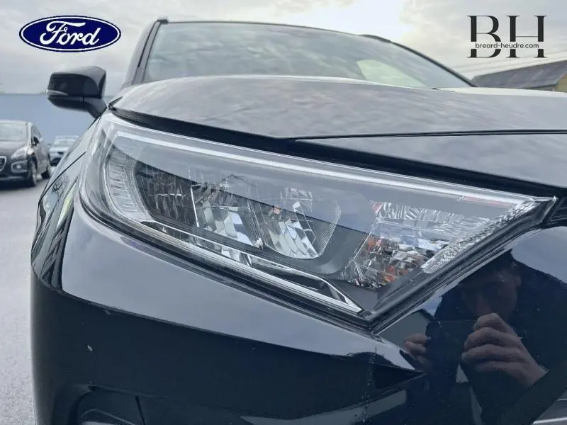 Gros plan sur le phare avant gauche du Toyota RAV4 noir métallisé, mettant en valeur son design anguleux et moderne.